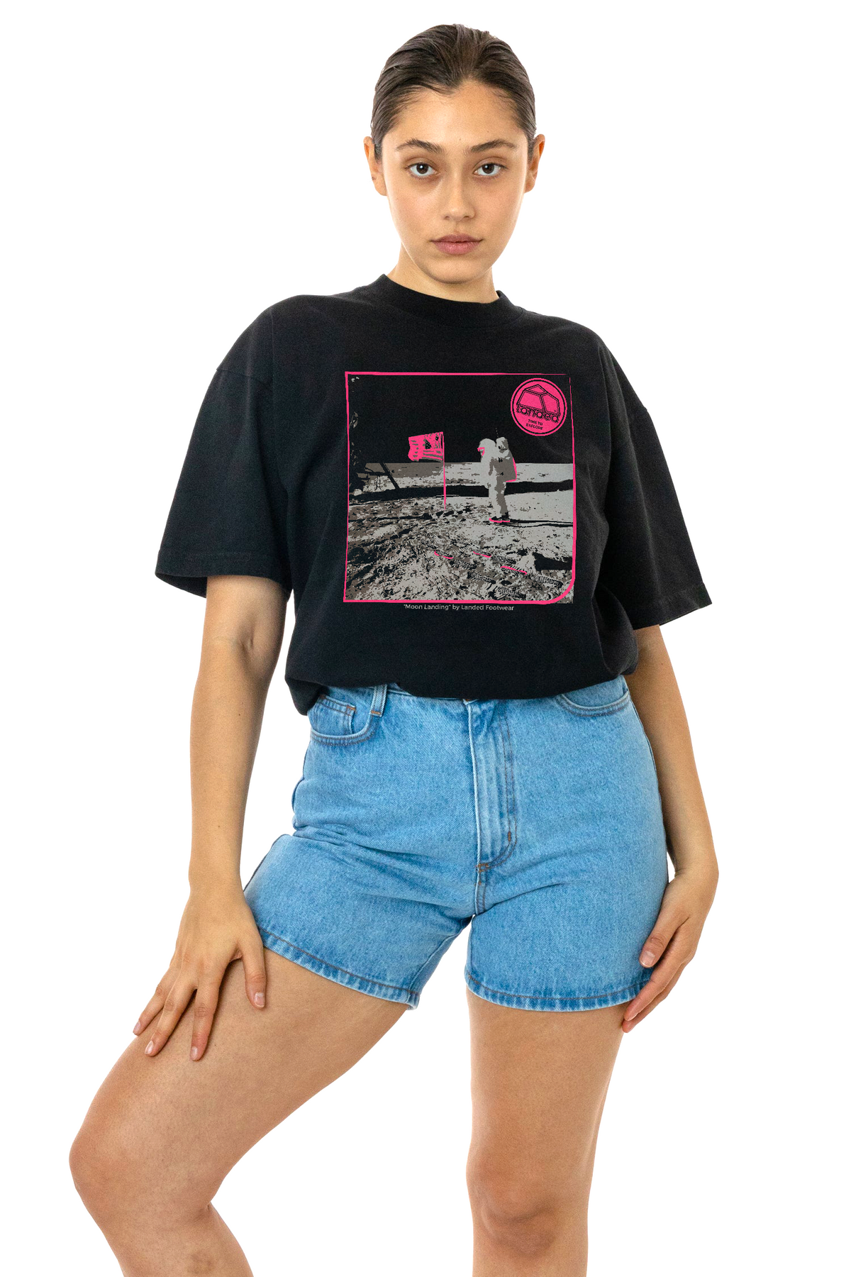 Landed black cotton t-shirt featuring a pink moon landing graphic print worn by a model with blue denim shorts