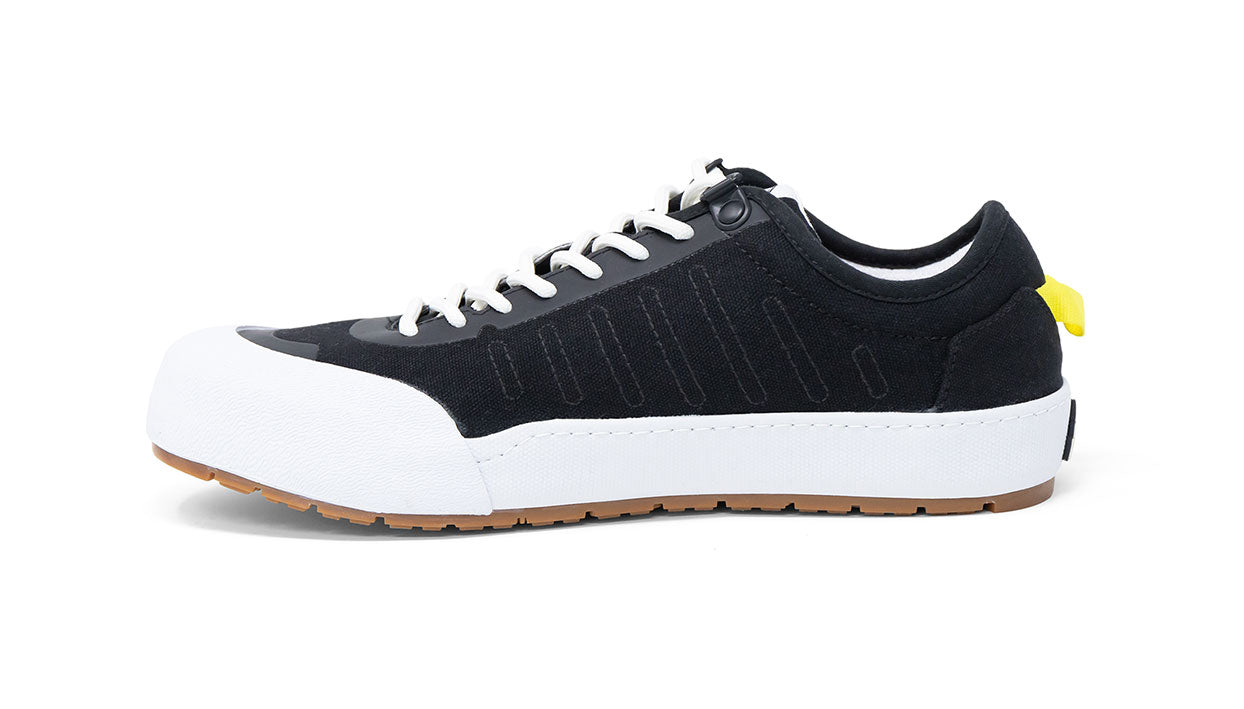 Landed The Overlook 1.0 black technical sneaker with white rubber toe cap, white laces, and yellow heel pull tab.