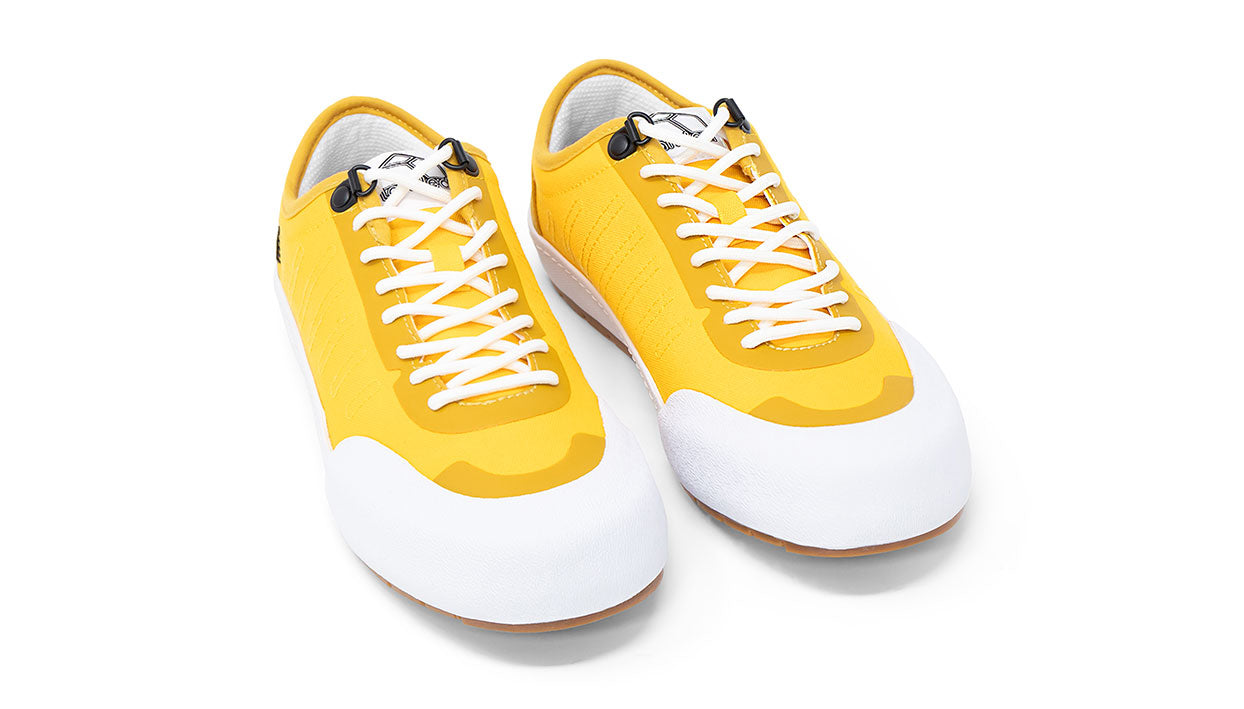 Landed The Overlook 1.0 yellow technical sneakers with white rubber toe caps and white laces on a white background.